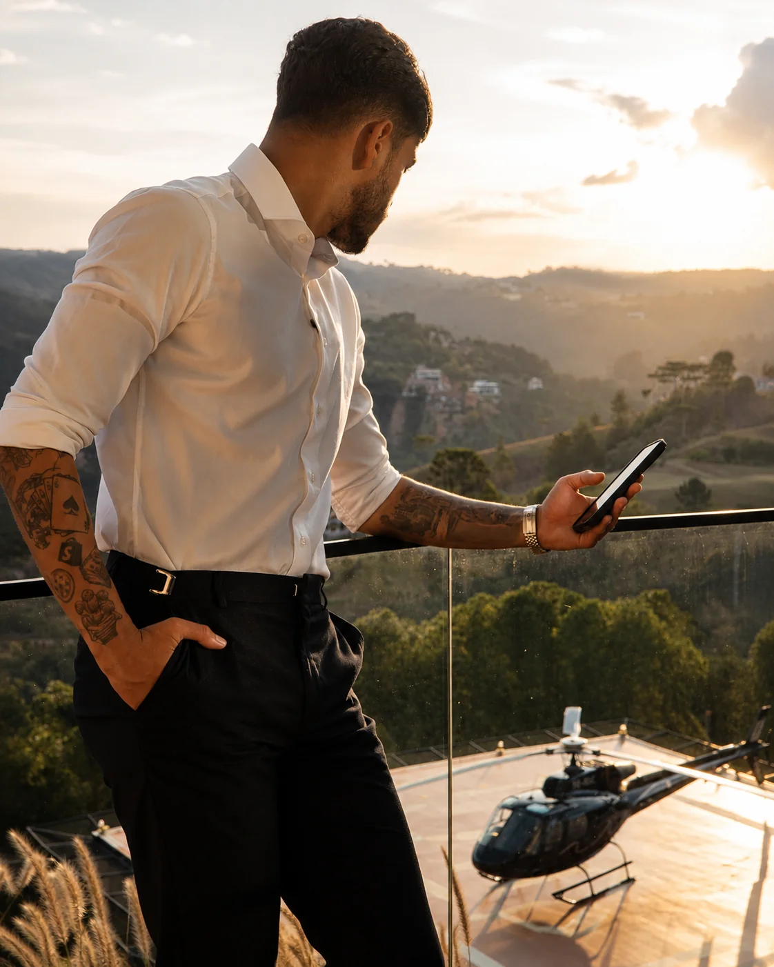 Douglas Rodrigues observando o celular ao pôr do sol, com helicóptero ao fundo